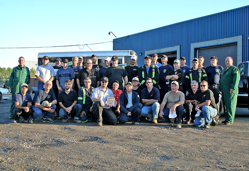 Group photo of Ottawa Metro Towing staff members standing in front of a blue industrial building and service vehicles