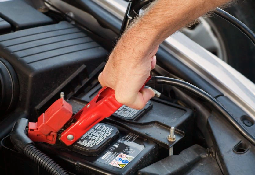 Technician connecting jumper cables to a car battery for boosting service