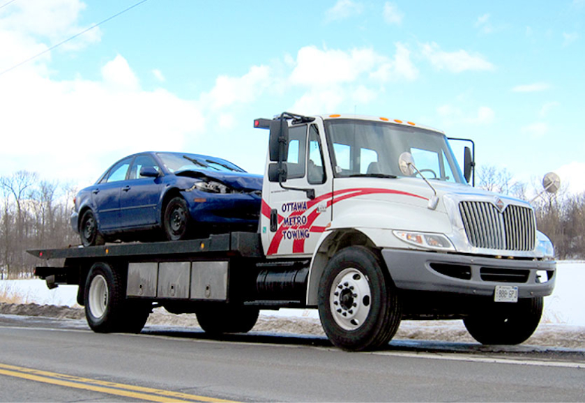 Ottawa Metro Towing flatbed truck carrying a damaged blue car in winter conditions