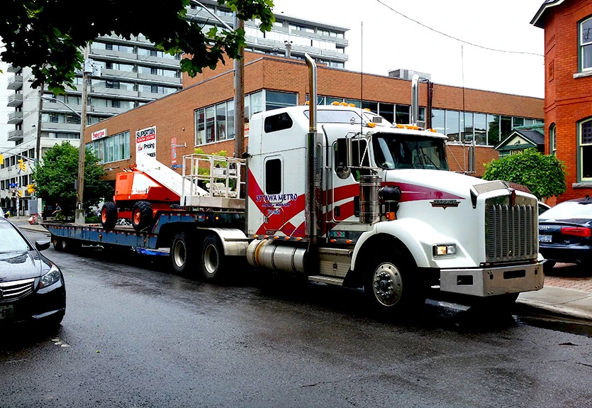 Heavy duty Ottawa Metro Towing truck transporting construction equipment through city street