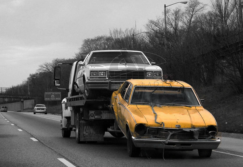 Flatbed tow truck transporting two vintage cars, one white and one yellow taxi, on a highway